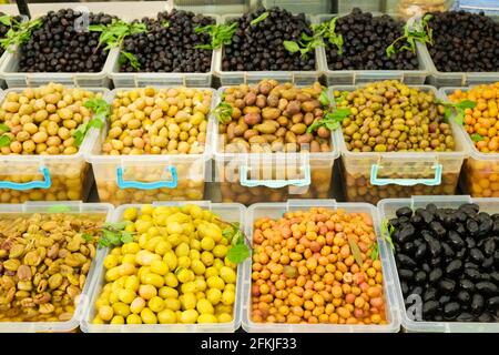 Mehrere Plastikbehälter mit Haufen reifer organischer gemischter griechischer Oliven (schwarz, grün, gelb) in Öl stehen im Supermarkt/Supermarkt auf dem Display Stockfoto
