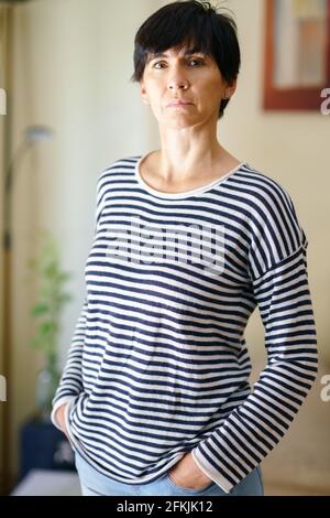 Frau mittleren Alters, die zu Hause posiert und die Kamera mit Gelassenheit anschaut. Stockfoto
