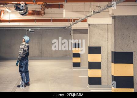 Kaukasischer Luftzirkulation Techniker in den 40ern, der die Entfernung verschmutzter Luft in einer neuen Tiefgarage überprüft, die an einer Garagendecke installiert ist. Sie Industriell Stockfoto