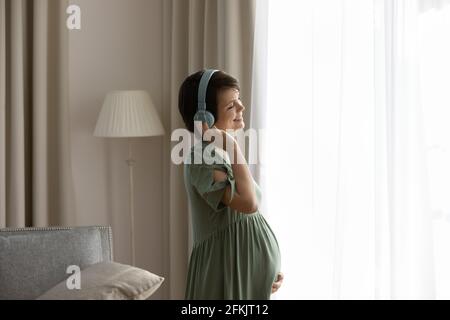 Lächelnde Schwangere in Kopfhörern hören Musik Stockfoto