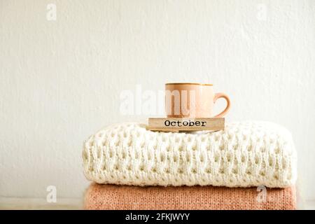 Wort oktober geschrieben auf Holzkalender, Cappuccino-Kaffeetasse, Bund von gestrickten warmen Pullover mit verschiedenen Strickmuster im Stapel gefaltet. Fallen Stockfoto