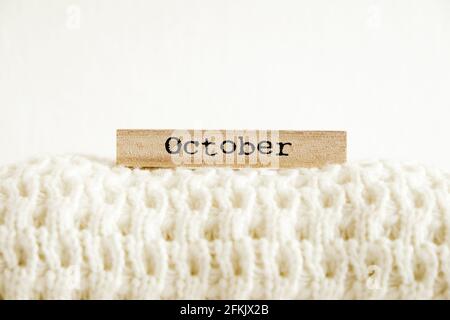 Wort oktober auf Holzkalender geschrieben, gestrickt warmweißen Pullover mit sichtbaren Strickmuster ordentlich gefaltet. Herbst / Winter Saison Strickmode Clothiswear Stockfoto