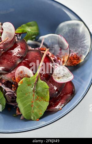 Rüben-Sommersalat mit Rucola, Radicchio, Weichkäse und Walnüssen auf Tellerdressing und Gewürzen auf blauem Teller, Kopierraum, Draufsicht. Stockfoto