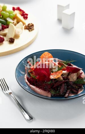 Rüben-Sommersalat mit Rucola, Radicchio, Weichkäse und Walnüssen auf Tellerdressing und Gewürzen auf blauem Teller, Kopierraum, Draufsicht. Stockfoto