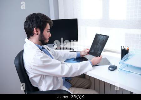 Junger Arzt untersucht Röntgenaufnahmen von Hüften und Wirbelsäule auf Rückenschmerzen. Radiographie einer Beckenzone. Stockfoto