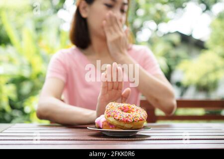 Die schöne asiatische gesunde Frau mittleren Alters sitzt auf dem Balkon neben dem Garten und weigert sich, die Nuss zu essen. Konzept der Gesundheitsversorgung und Ernährung Stockfoto