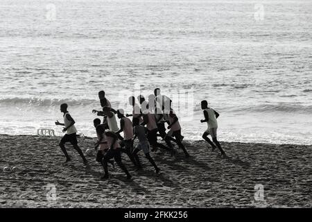 Junge männliche Spieler haben am Strand neben der Wasserlinie des Ozeans ein Fußballteam-Training mit Silhouetten gemacht. Stockfoto