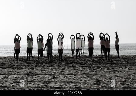 Junge männliche Spieler haben am Strand neben der Wasserlinie des Ozeans ein Fußballteam-Training mit Silhouetten gemacht. Stockfoto