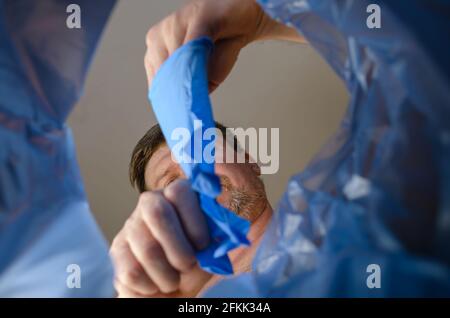 Eine Hand schmeißt blaue medizinische Handschuhe in einen Mülleimer.man entfernt Schutzhandschuhe aus der Hand über den Müllkorb. Ansicht von unten. In Innenräumen. Stockfoto