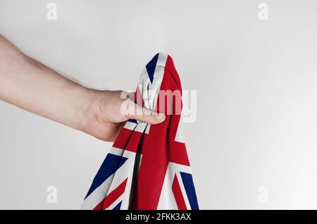 Staatsflagge Großbritanniens in der Hand auf weißem Hintergrund. Ein Mann hält die Flagge des Vereinigten Königreichs von Großbritannien und Nordirland. Seitenansicht Stockfoto