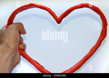 Herz aus Pappe in der Hand eines Mannes. Ein Symbol des Herzens aus rotem Papier auf weißem Hintergrund. Papierherz. Stockfoto