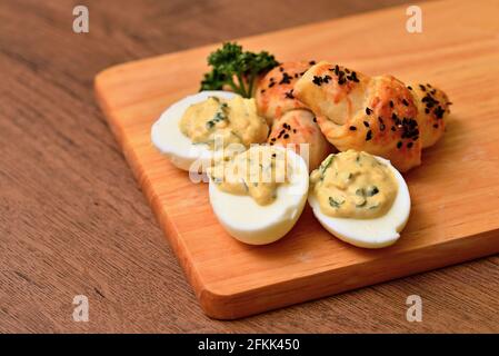 Eier Mimosa Käse Mini-Croissant auf einem Holzbrett. Eier und Gebäck mit einem Zweig lockiger Petersilie arrangiert. Eier gefüllt mit Creme, hausgemachte Pasta Stockfoto