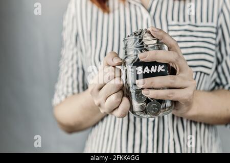 Person hält Münzen im Glasgefäß. Ersparnisse zur Deckung von Hypotheken oder Bankdarlehen.Flasche mit Aufkleber in den Händen. Konzept der Ertrags- und Finanzkompetenz und zivilrechtlichen Haftung. Stockfoto
