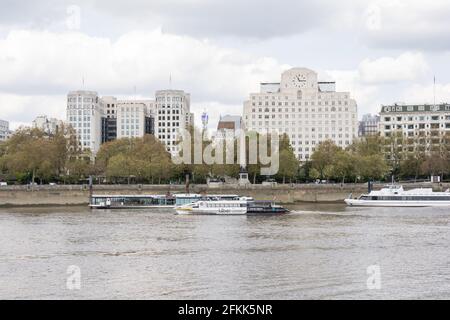 Ein Thames Clipper Uber Boot, das vor dem Shell House und der Cleopatra's Needle auf dem Victoria Embankment, London, England, Großbritannien, vorbeifährt Stockfoto