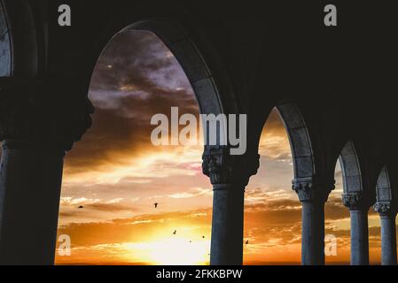 Ein faszinierender Blick auf die Vögel, die während des Sonnenuntergangs fliegen Vom Torbogen aus Stockfoto