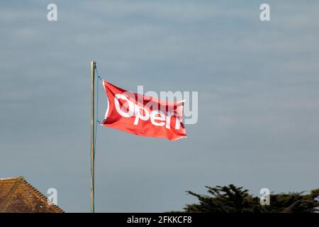 „Offene“ Flagge weht im Wind. Ein kleines lokales Unternehmen teilt seinen Kunden mit, dass sie nach der Sperre von covid-19 2021 wieder für Geschäfte geöffnet sind Stockfoto