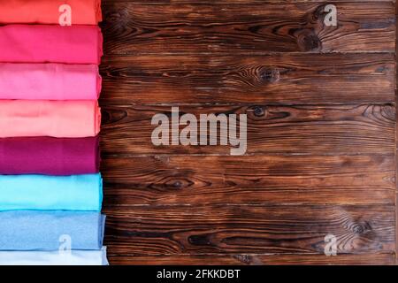 Nahaufnahme von farbenfrohen Kleidern, die ordentlich gerollt sind, um Platz im Gepäck zu sparen, Stapel von Baumwoll-T-Shirt-Rollen in verschiedenen Pastellfarben auf Holztexturtisch. Stockfoto