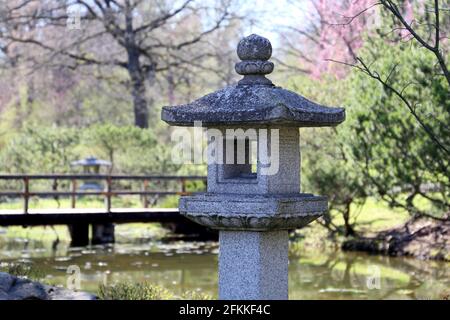 Japanischer Garten im Frühling, orientalische Kultur. Alte Tachi-gata Steinlaterne, Teich und Brücke umgeben von Bäumen Stockfoto