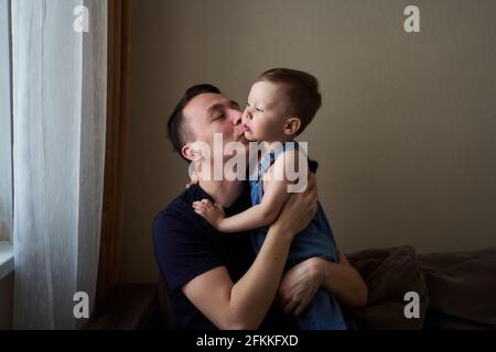 Vater hält seinen kleinen Sohn in den Armen und küsst ihn im Freien. Glückliche Familie und Vater Pflege Konzept. Stockfoto