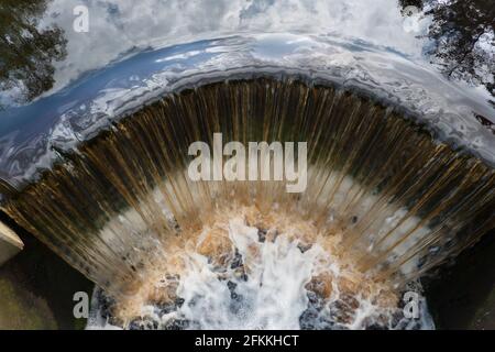 Draufsicht auf braunes, eisenreiches Wasser, das über ein Wehr fällt Stockfoto