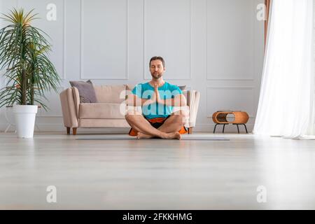 Foto eines Mannes mittleren Alters zu Hause. Er sitzt in der Lotusposition mit Kopfhörern und hört Meditationsmusik. Workout zu Hause. Stockfoto