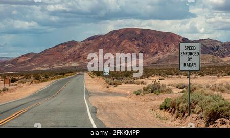 Geschwindigkeitsbegrenzung 55 MPH. Geschwindigkeit durch Radar erzwungen. Warnschilder auf einem Wüstenautobahn. Nevada, USA, leere, landschaftlich schöne Asphaltstraße, wolkig-himmelverdeckter Rückweg Stockfoto