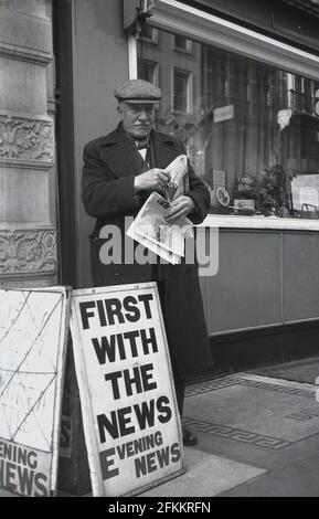 1950, historisch, ein älterer männlicher Zeitungsverkäufer, in Mantel und Stoffkappe, der draußen auf einem Bürgersteig stand, der die Evening News verkauft, London, England, Großbritannien. Stockfoto