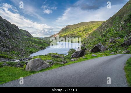 Wunderschöne Landschaft mit See, grünen Hügeln und kurvenreicher Straße in Gap of Dunloe, Black Valley, MacGillycuddys Reeks Mountains, Ring of Kerry, Irland Stockfoto