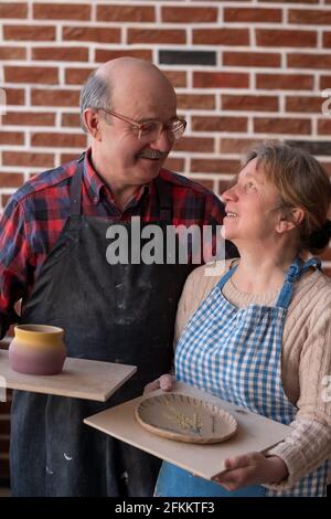 Ein älterer Mann und eine ältere Frau halten nach dem Workshop handgemachten Topf und Teller in der Hand Stockfoto