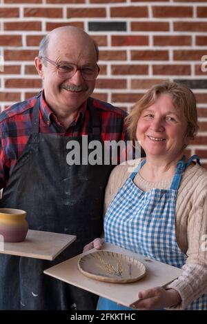 Ein älterer Mann und eine ältere Frau halten nach dem Workshop handgemachten Topf und Teller in der Hand Stockfoto