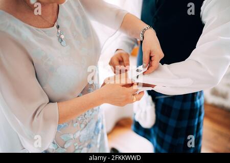 Vorbereitung auf eine schottische Hochzeit. Frau, die Manschettenknöpfe auf einem Hemd eines Mannes im Kilt befestigt Stockfoto
