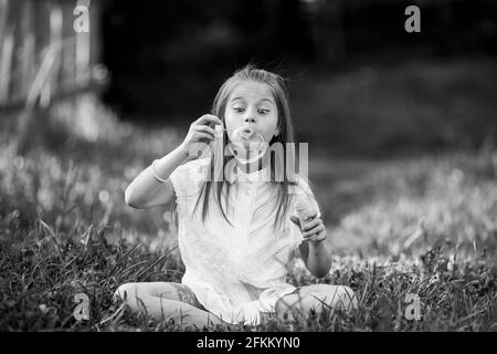 Ein kleines Mädchen bläst im Freien emotional Seifenblasen auf. Schwarzweiß-Foto. Stockfoto