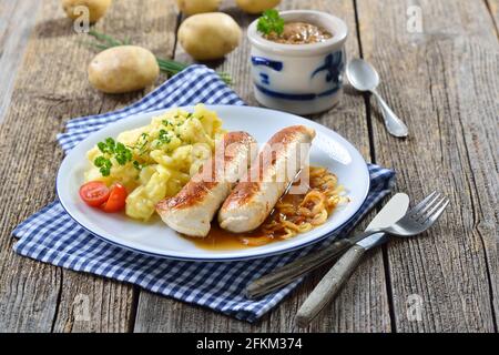 Gebratene bayerische Würstchen, sogenannte Wollwurst, eine Spezialität ähnlich der deutschen Kalbswurst, aber ohne Gehäuse, serviert mit Kartoffelsalat und Soße Stockfoto