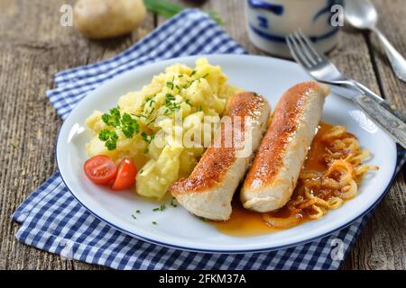 Gebratene bayerische Würstchen, sogenannte Wollwurst, eine Spezialität ähnlich der deutschen Kalbswurst, aber ohne Gehäuse, serviert mit Kartoffelsalat und Soße Stockfoto