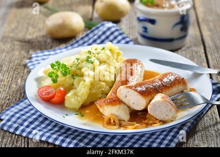 Gebratene bayerische Würstchen, sogenannte Wollwurst, eine Spezialität ähnlich der deutschen Kalbswurst, aber ohne Gehäuse, serviert mit Kartoffelsalat und Soße Stockfoto