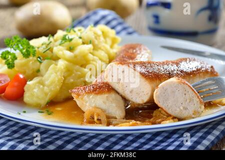 Gebratene bayerische Würstchen, sogenannte Wollwurst, eine Spezialität ähnlich der deutschen Kalbswurst, aber ohne Gehäuse, serviert mit Kartoffelsalat und Soße Stockfoto