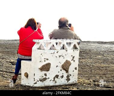 Ein nicht erkennbares älteres Paar, das auf einer Bank sitzt und fotografiert Die Seestücke mit Smartphones Stockfoto