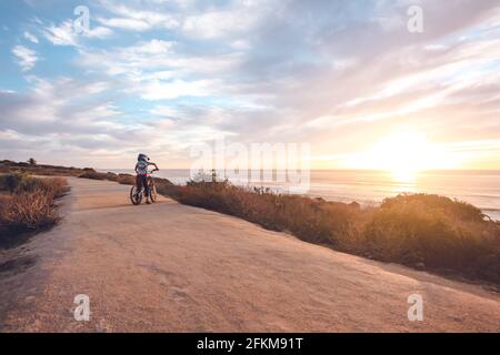 Der Junge trägt ein T-Shirt und fährt mit dem Fahrrad auf einem Küstenpfad. Stockfoto