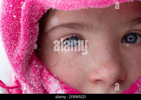 Eine Nahaufnahme eines Mädchens, das für den Winter gekleidet ist Schneeflocken in ihren Wimpern Stockfoto