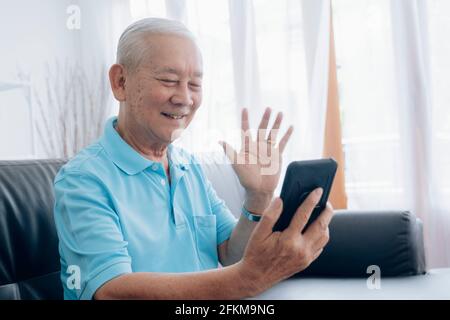 Älterer Mann, der Videoanruf abgibt und auf dem Bildschirm winkt. Stockfoto