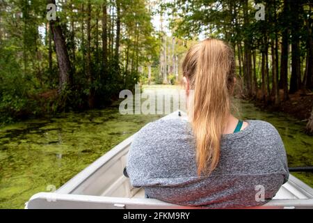 Eine blonde Schwanzschwänze, die in einem weißen Boot sitzt, das in einem Sumpf in Moncks Corner, South Carolina, schwimmt Stockfoto