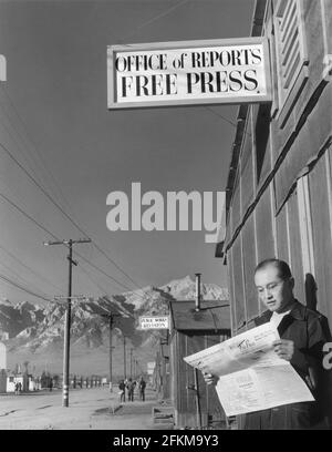 Der Herausgeber Roy Takeno liest eine Kopie der Manzanar Free Press vor dem Zeitungsbüro, dem Manzanar Relocation Center, Kalifornien, USA, Ansel Adams, Manzanar War Relocation Center Collection, 1943 Stockfoto