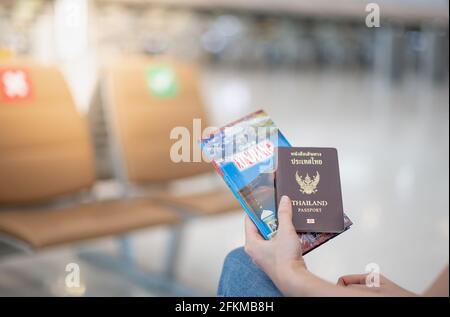 Weibliche Hand hält Thailand Passbuch und Reiseführer Buch am Flughafen, aufgrund der Covid-19 Epidemie Pandemie Konzept. Stockfoto