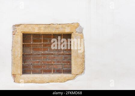 Das Fenster ist mit Ziegeln und Balken zugemauert. An der weißen Wand ist ein Fenster mit Balken. Stockfoto
