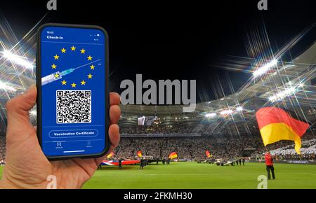 FOTOMONTAGE, Hand hält Smartphone mit digitalen europäischen Impfkarte im Fußballstadion mit Zuschauern, symbolisches Bild, Corona-Krise Stockfoto