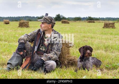 hunter mit seinem Schützenhund, der während des auf dem Heufeld ruht Herbstjagd Stockfoto