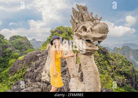 Frau Tourist auf dem Hintergrund der erstaunlichen riesigen Drachenstatue auf Kalkstein Berggipfel in der Nähe Hang Mua Aussichtspunkt am nebligen Morgen. Beliebter Tourist Stockfoto