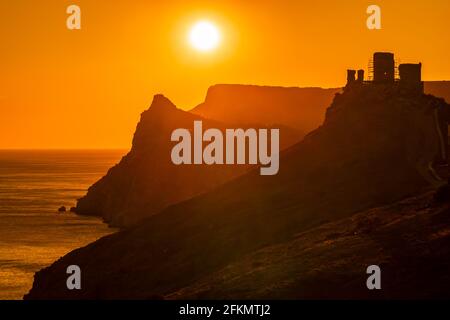 Ein rot brennender Sonnenuntergang mit dem Silhouett einer Klippe Und Burg über dem Meer Stockfoto