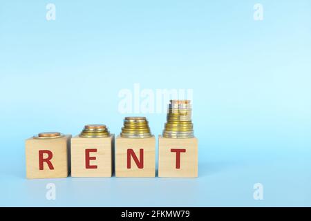 Mieterhöhung Konzept. Wortmiete auf Holzblöcken in blauem Hintergrund mit zunehmendem Münzstapel. Stockfoto