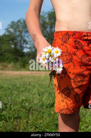 Ein kleiner Strauß Wildblumen in den Händen eines Jungen. Temporäre Tätowierung auf der Hand eines Kindes. Bouquet von Gänseblümchen. Stockfoto